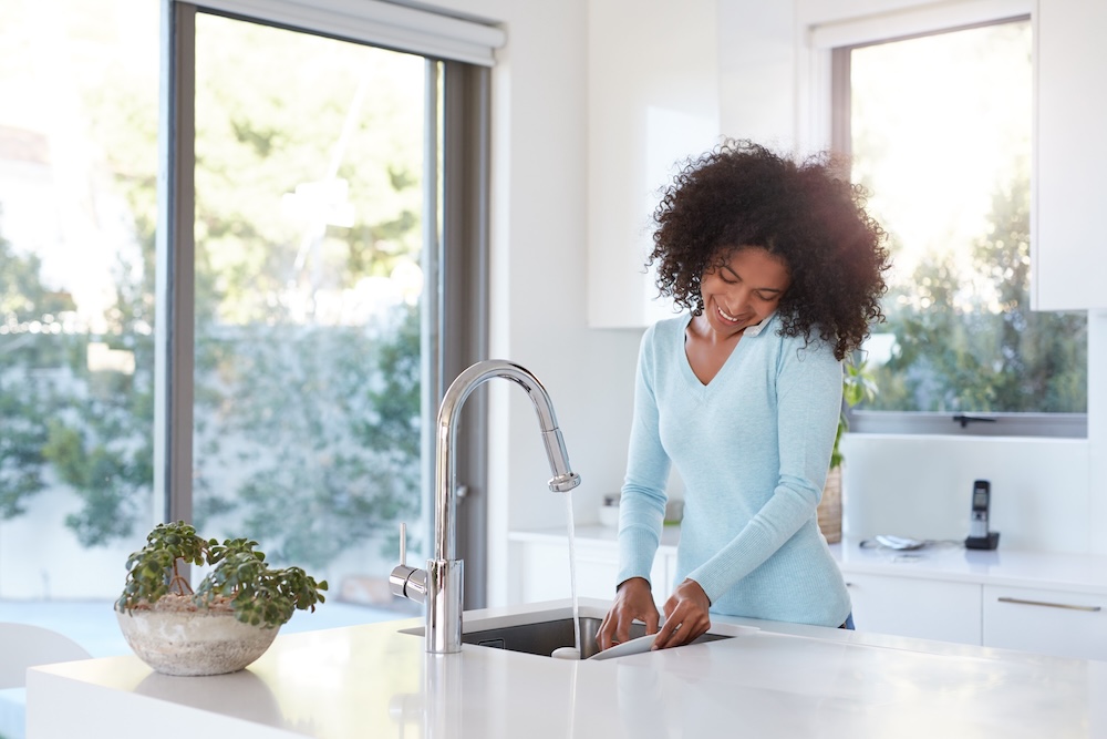 Shot of a young woman talking on her cellphone while washing the dishes
